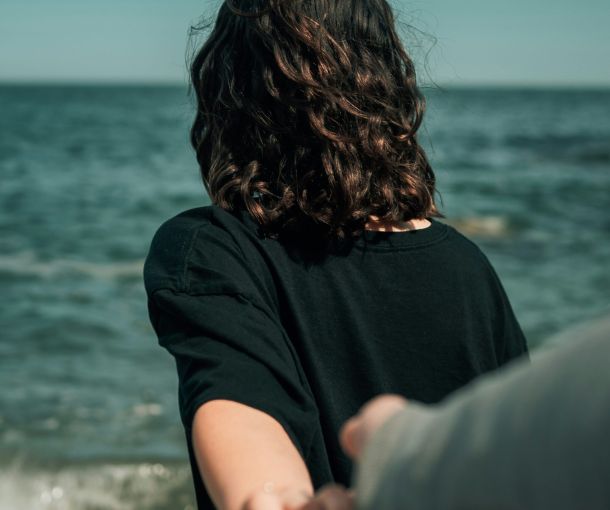 A couple stands on the beach, holding hands with one partner looking away, representing neurodiversity and relationships.