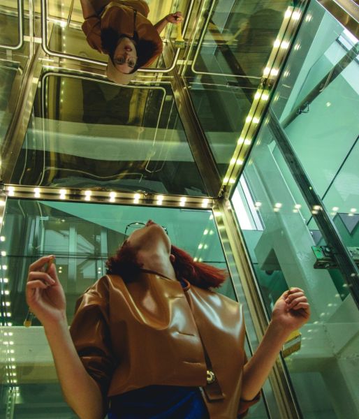 A woman in a glass elevator looks up at her reflection representing the self-discovery process during an adult autism assessment.