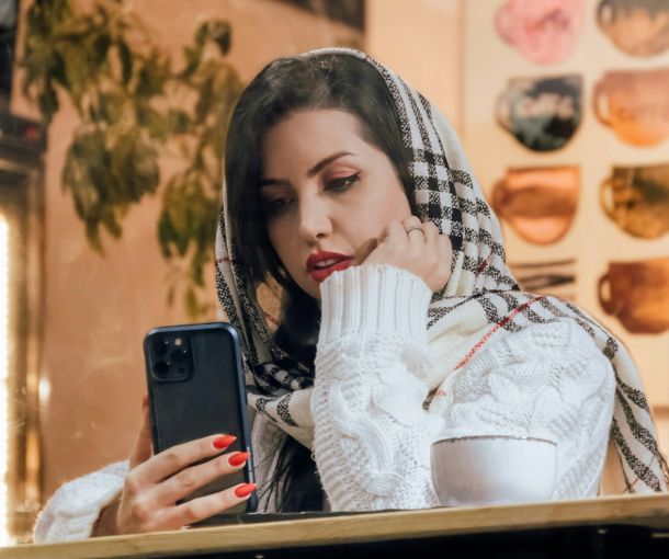 A woman wearing a scarf looks at her phone, considering her out-of-network benefits and insurance reimbursement details.