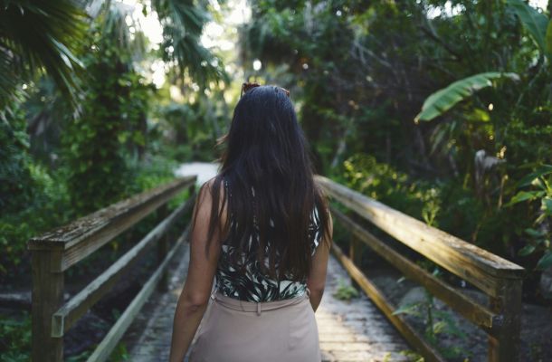 A woman with long dark hair walking over a bridge into her new life, symbolizing post-diagnosis coaching for autistic adults at NeuroSpark Health.