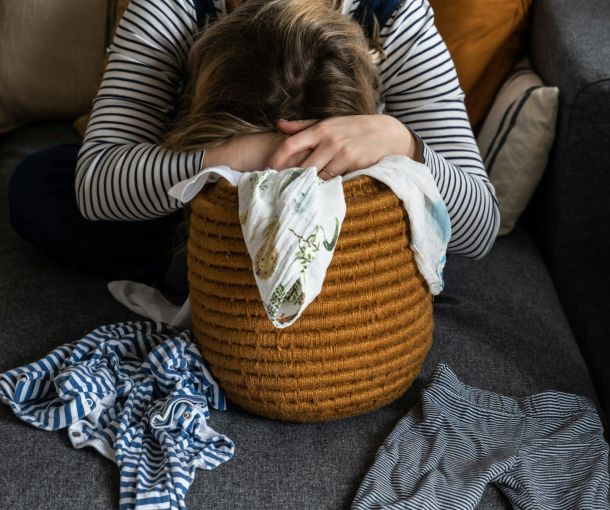 A woman sits on a couch hiding her face with her hands, reflecting feelings of stress and the challenges of pathological demand avoidance (PDA).