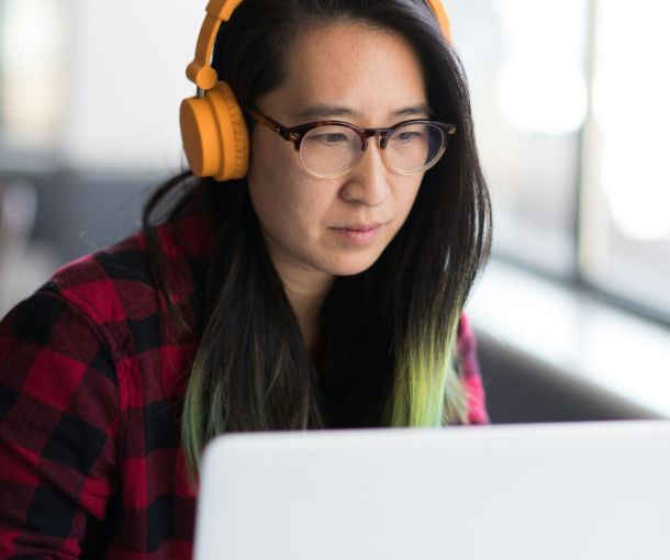 A woman with orange headphones focuses on her computer, representing neurodiversity at work.